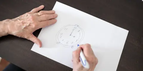 Mani anziane disegnano un orologio su carta, parte di un test memoria anziani.