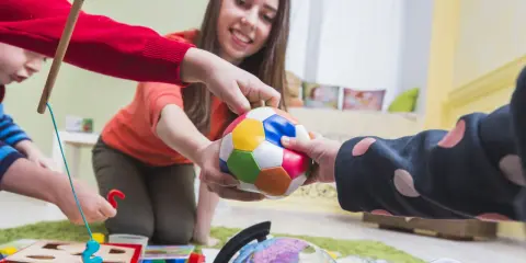 Bambini e terapista giocano con una palla colorata, un globo e un gioco di incastri. La terapia occupazionale cos'è? È questo: gioco e apprendimento.