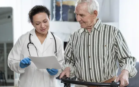 Medico spiega a paziente anziano con deambulatore il significato di un problema cognitivo, mostrando un documento.