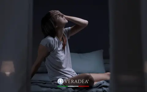 Donna sveglia di soprassalto nel letto, con la mano sulla fronte, soffre di sudorazione notturna. Cerca rimedi per dormire serenamente.