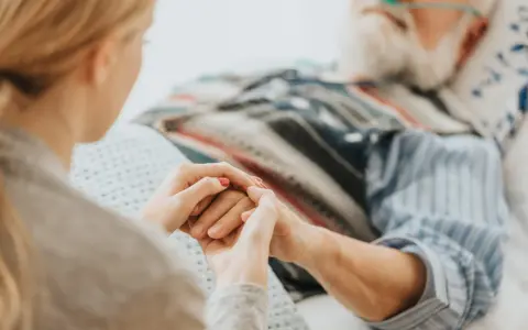 Mani che si stringono tra una giovane donna e un anziano in ospedale. Scopri cosa spetta a chi assiste un familiare con la 104.