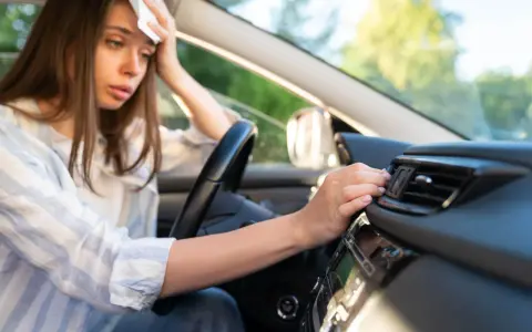 Donna in auto, con un fazzoletto sulla fronte, soffre di sudorazione eccessiva al minimo sforzo, cercando sollievo vicino alla bocchetta dell'aria.