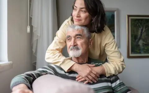 Un uomo anziano con Alzheimer, abbracciato da una donna, sembra cogliere un momento di lucidità, un ricordo che riaffiora.