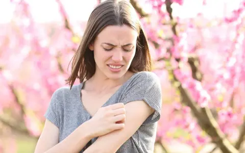 Donna con prurito in tutto il corpo la sera, graffiandosi il braccio tra i fiori rosa.