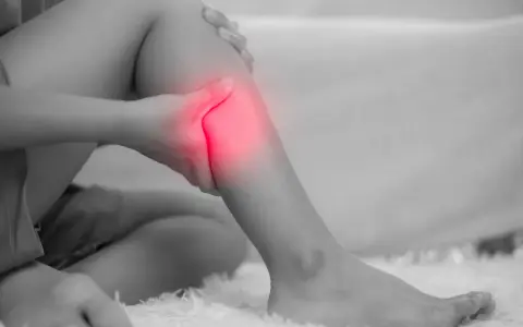 Donna che si tiene la gamba, evidenziata in rosso, a causa di dolori alle gambe, un possibile problema neurologico.