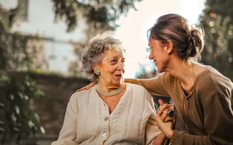 Una donna accarezza la spalla di un'anziana, un gesto di affetto che può alleviare i sintomi della demenza senile avanzata.