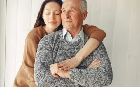 Un abbraccio affettuoso: un modo per come calmare una persona con demenza senile. La giovane donna stringe dolcemente l'anziano uomo, offrendo conforto e sicurezza.