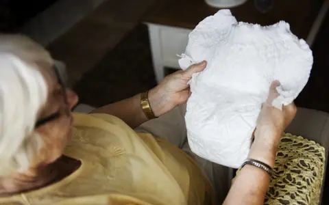 Anziana tiene in mano un prodotto per l'igiene intima, una possibile alternativa al pannolone per anziani, valutandone la morbidezza.