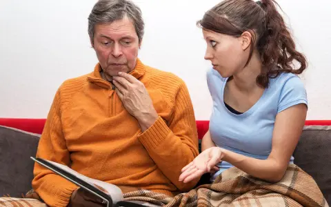 Uomo con espressione preoccupata guarda un album, mentre una donna gli parla con fare interrogativo. Potrebbe trattarsi di demenza senile precoce sintomi.