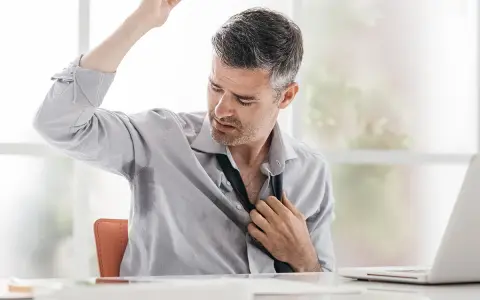 Uomo d'affari con camicia bagnata di sudore sotto le ascelle, che si sbottona la cravatta. Le cause del sudare freddo sono molteplici.