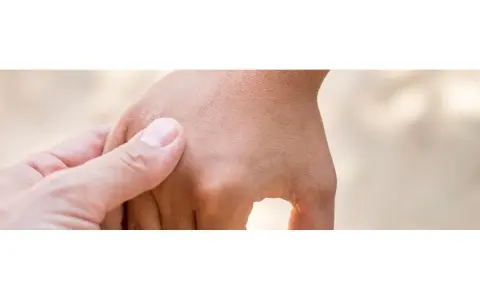 Mano adulta che accarezza delicatamente la mano di un bambino, notando una lieve irritazione cutanea che potrebbe far pensare a una falsa scabbia.