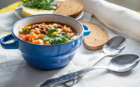 Zuppa nutriente, ideale per una dieta per anziani over 90. Servita in ciotola blu con pane integrale e erbe fresche.