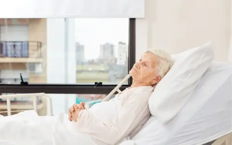 Anziana allettata in ospedale, con mani giunte. La domanda "quanto può vivere un anziano allettato" è complessa e dipende da molti fattori.