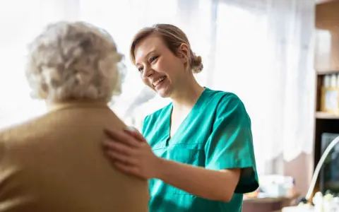 Infermiera sorridente incoraggia un'anziana con difficoltà a parlare, offrendo supporto e comprensione.
