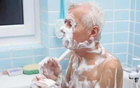 Un anziano con Alzheimer, coperto di schiuma, si lava. Un gesto di cura per convincerlo a lavarsi.