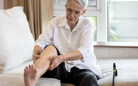 Anziano con gambe gonfie cerca rimedi, massaggiando la caviglia.