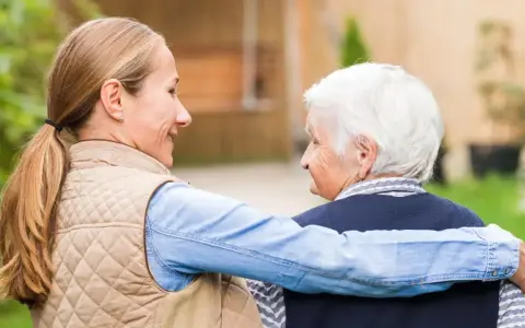 Giovane donna abbraccia un'anziana, offrendo supporto e affetto, un gesto di cura che può aiutare a contrastare la demenza senile.