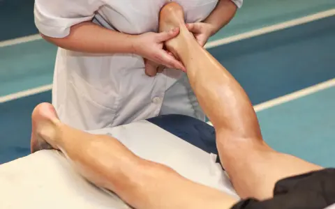 Mani esperte eseguono un massaggio trasverso profondo alla caviglia e al polpaccio di un atleta, alleviando la tensione muscolare.