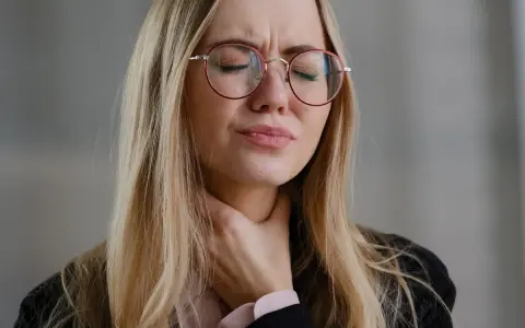Donna con occhiali rossi si stringe la gola, visibilmente sofferente. Cerca rimedi per un prurito insopportabile.