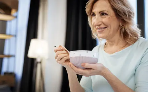 Donna sorride mentre mangia una zuppa cremosa, un esempio di cosa mangiare con disfagia.