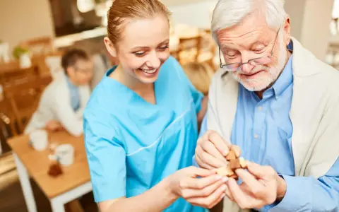 Assistente sorridente aiuta un anziano con demenza a completare un puzzle, mostrando come le fissazioni possano essere gestite con pazienza e attività stimolanti.
