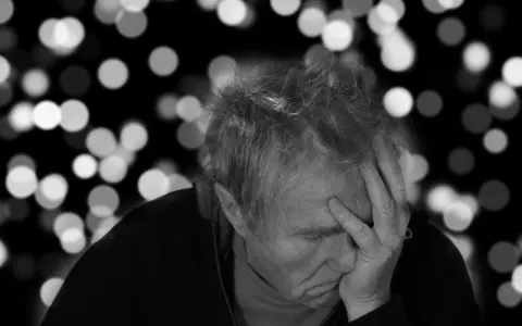 Uomo anziano con mano sulla fronte, pensieroso. L'Alzheimer può manifestarsi a diverse età, ma è più comune dopo i 65 anni.