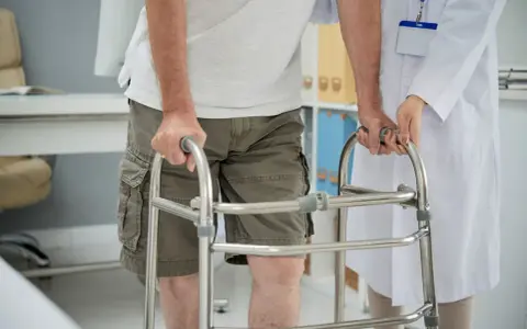 Paziente con problemi di deambulazione che si appoggia a un deambulatore, assistito da un medico.