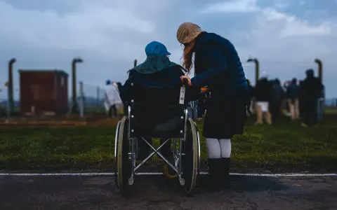 Accompagnamento anziani a chi spetta: una donna spinge una persona in sedia a rotelle, con altre figure sfocate sullo sfondo.