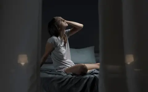Donna seduta a letto, con la mano sulla fronte, soffre di sudore notturno al collo.