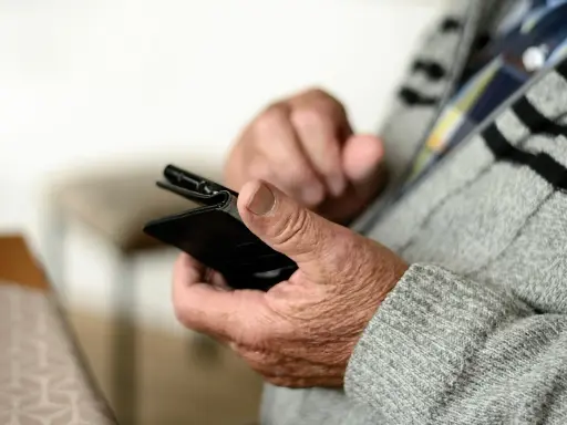 Mani anziane che tengono uno smartphone, forse per capire come fare lo SPID.