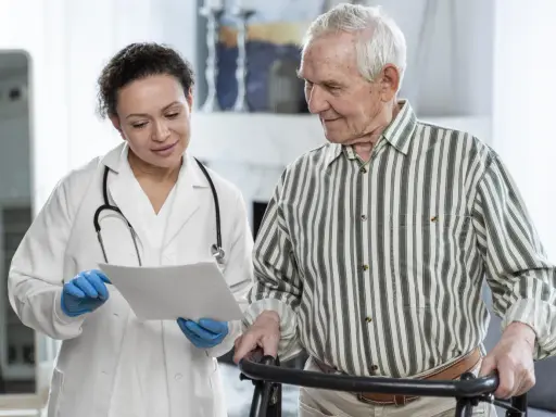 Medico spiega a paziente anziano con deambulatore il significato di un problema cognitivo, mostrando un documento.