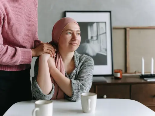 Una donna con un foulard rosa appoggiata a un'altra donna. Un esempio di cure palliative che offre conforto e supporto.