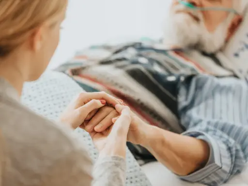 Mani che si stringono tra una giovane donna e un anziano in ospedale. Scopri cosa spetta a chi assiste un familiare con la 104.