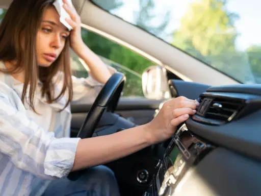 Donna in auto, con un fazzoletto sulla fronte, soffre di sudorazione eccessiva al minimo sforzo, cercando sollievo vicino alla bocchetta dell'aria.