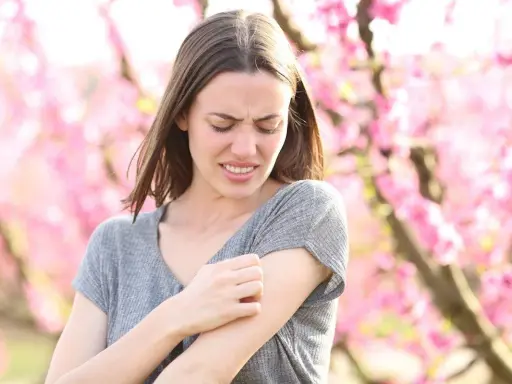 Donna con prurito in tutto il corpo la sera, graffiandosi il braccio tra i fiori rosa.