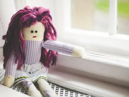 Bambola con capelli viola, vestita a quadretti, seduta sul davanzale. Un simbolo di conforto nella doll therapy per l'Alzheimer.