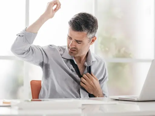 Uomo d'affari con camicia bagnata di sudore sotto le ascelle, che si sbottona la cravatta. Le cause del sudare freddo sono molteplici.