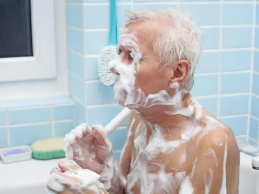 Un anziano con Alzheimer, coperto di schiuma, si lava. Un gesto di cura per convincerlo a lavarsi.