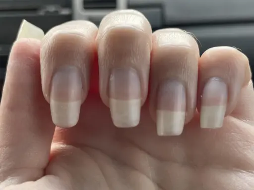 Dita con unghie curate, leggermente incurvate, che mostrano una french manicure naturale.