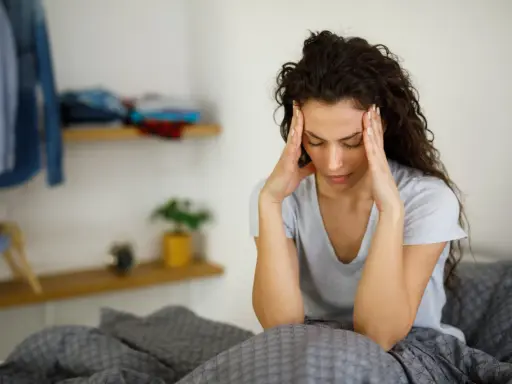 Donna con le mani sulle tempie, seduta a letto, soffre di giramenti di testa.