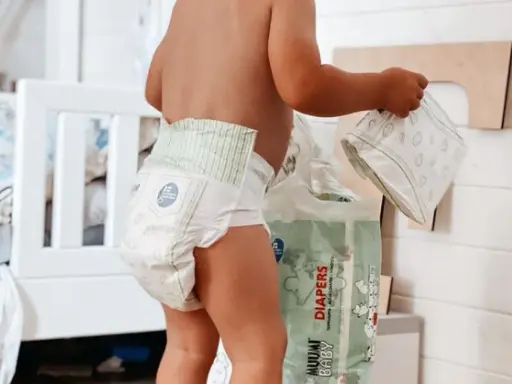 Un bimbo con un pannolino indosso, vicino a una confezione di pannolini. Sembra che i pannolini scadano, ma non c'è fretta.