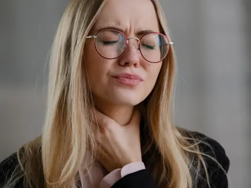 Donna con occhiali rossi si stringe la gola, visibilmente sofferente. Cerca rimedi per un prurito insopportabile.