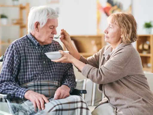 Una donna nutre con un cucchiaino il suo anziano nonno, che non mangia più, seduto su una sedia a rotelle.