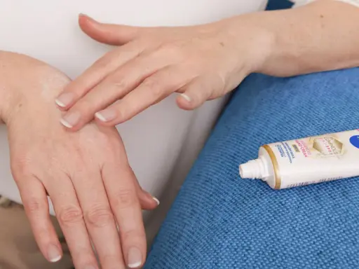 Mani che si massaggiano crema idratante per alleviare il prurito alle mani. Tubetto di Nivea Luminous 630 in primo piano.