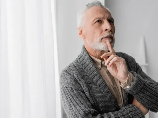 Uomo anziano con barba bianca, pensieroso, con un dito sul mento, forse valutando i risultati di un decadimento cognitivo test.