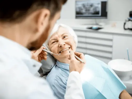 Un dentista esamina i denti di un'anziana sorridente, sottolineando l'importanza dell'igiene orale per gli anziani.