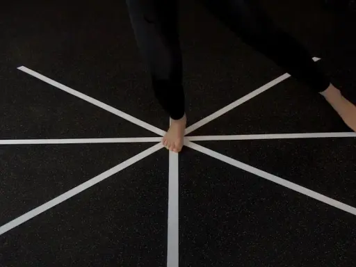 Persona esegue un test di equilibrio su un pavimento con nastro bianco a raggiera.
