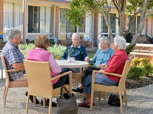 Anziani riuniti in giardino, chiacchierano e sorridono. Un momento sereno nella loro casa di riposo RSA.