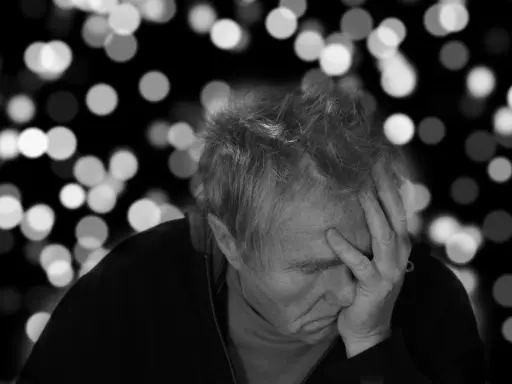 Uomo anziano con mano sulla fronte, pensieroso. L'Alzheimer può manifestarsi a diverse età, ma è più comune dopo i 65 anni.