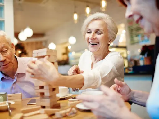 Anziani ridono giocando a Jenga, un esempio di iniziative per anziani che promuovono divertimento e socialità.
